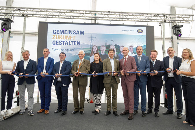Several people cut a blue ribbon at the opening of a new factory belonging to a resistor manufacturer